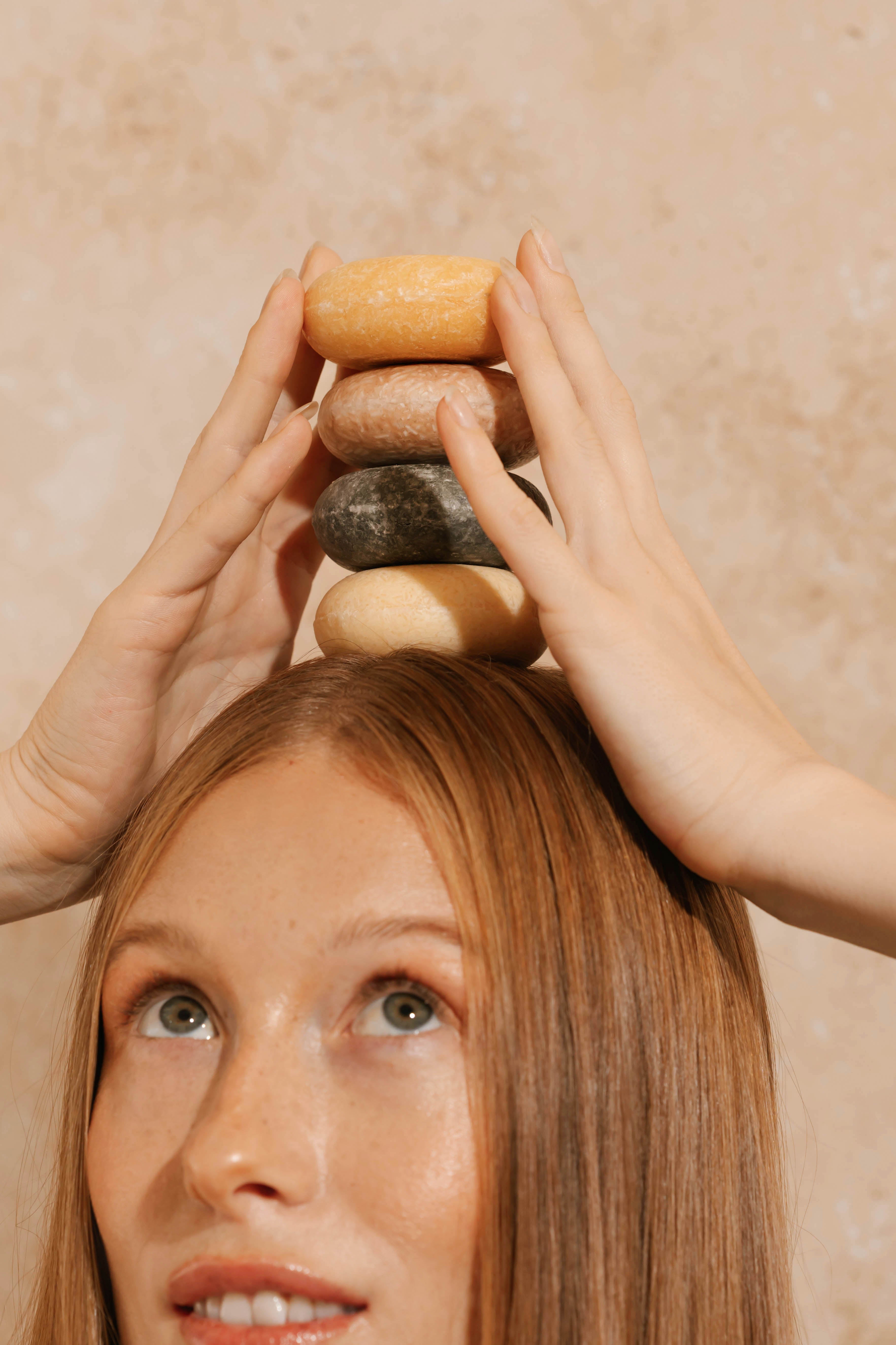 Person balancing a stack of hair care bars on their head with a neutral background