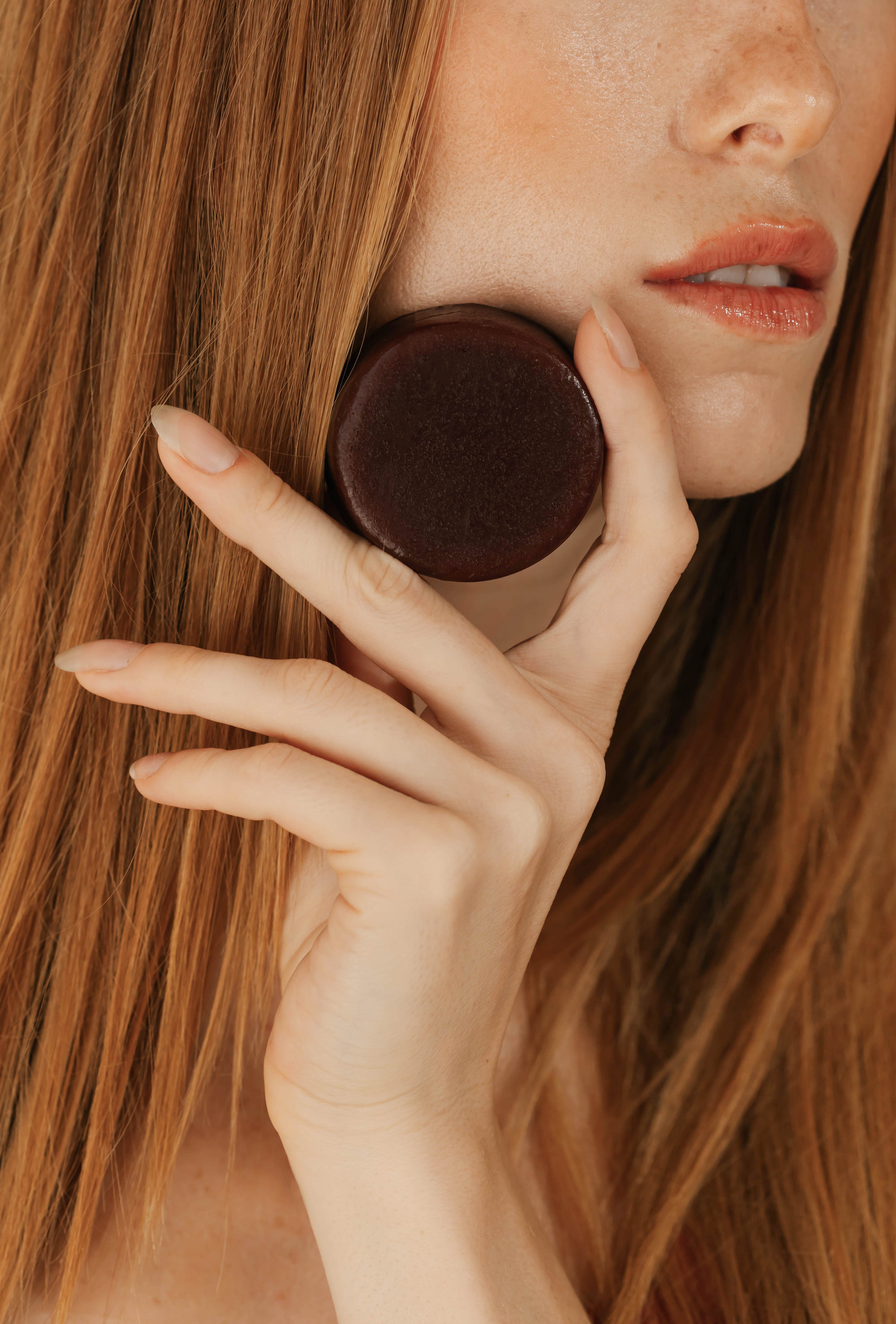 Close-up of a person holding a hair care bar against their cheek with a blurred background